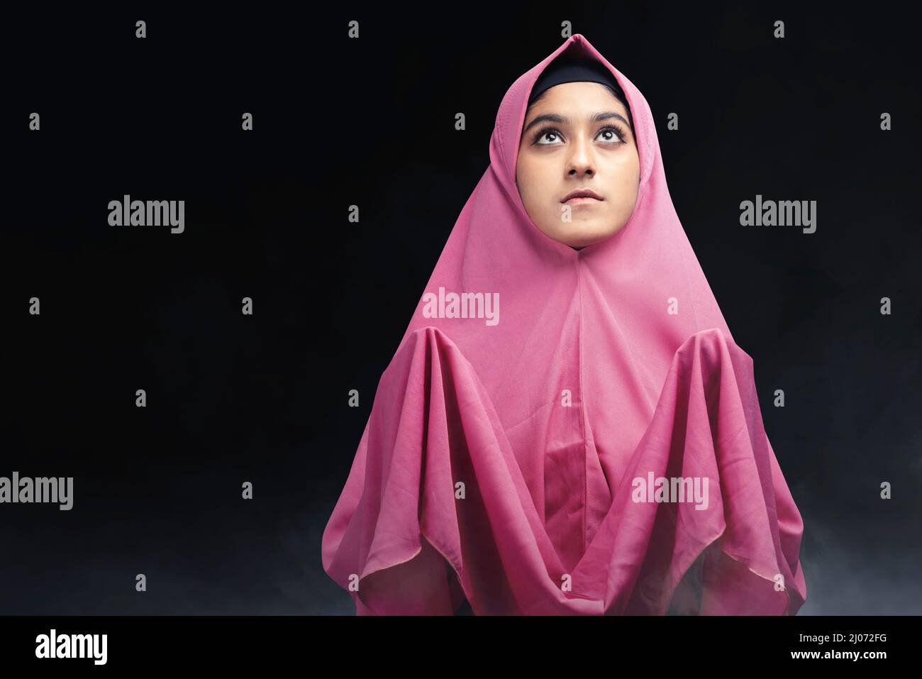 Asian Muslim woman in a veil standing while raised hands and praying ...