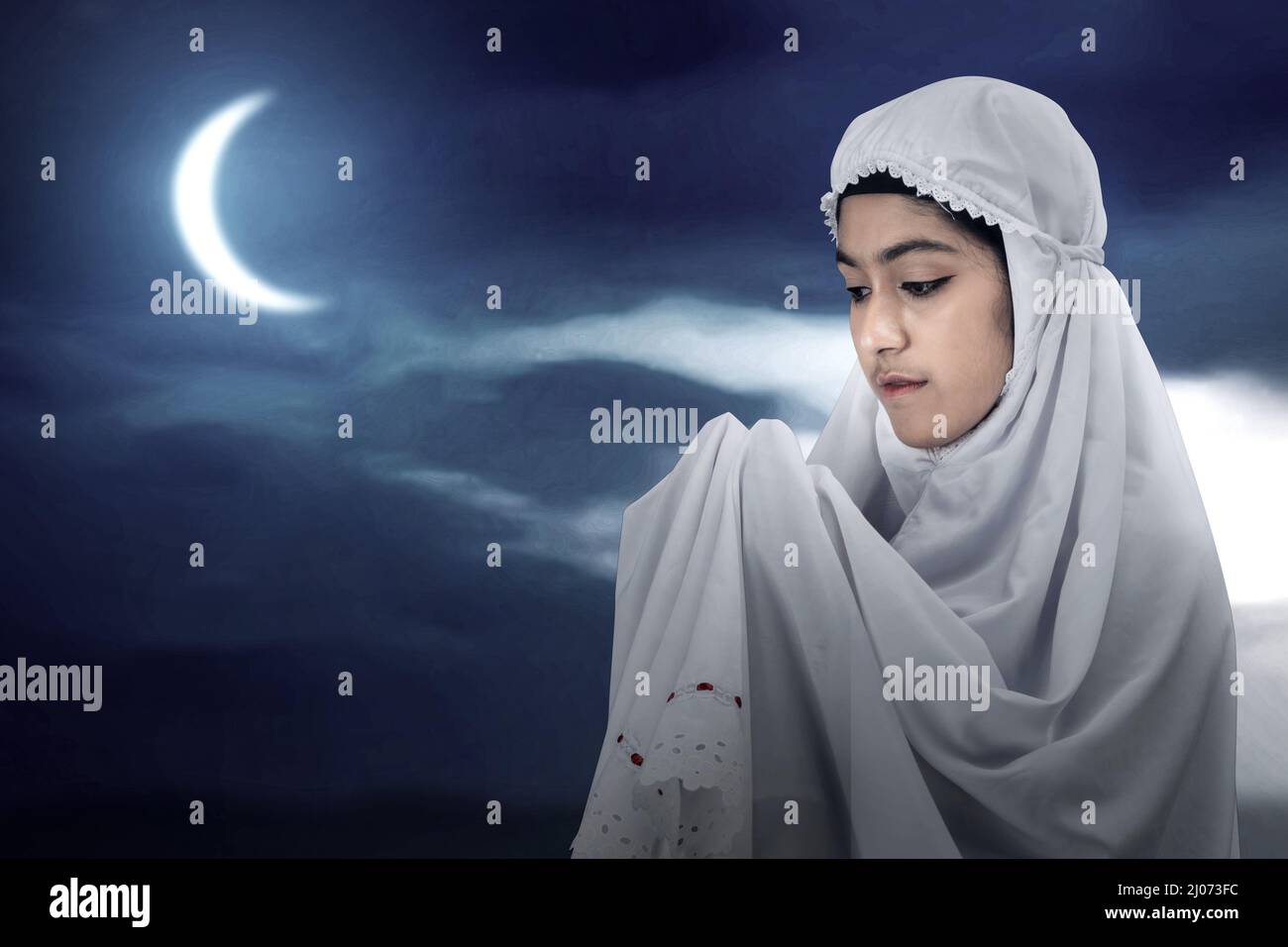 Asian Muslim woman in a veil standing while raised hands and praying ...