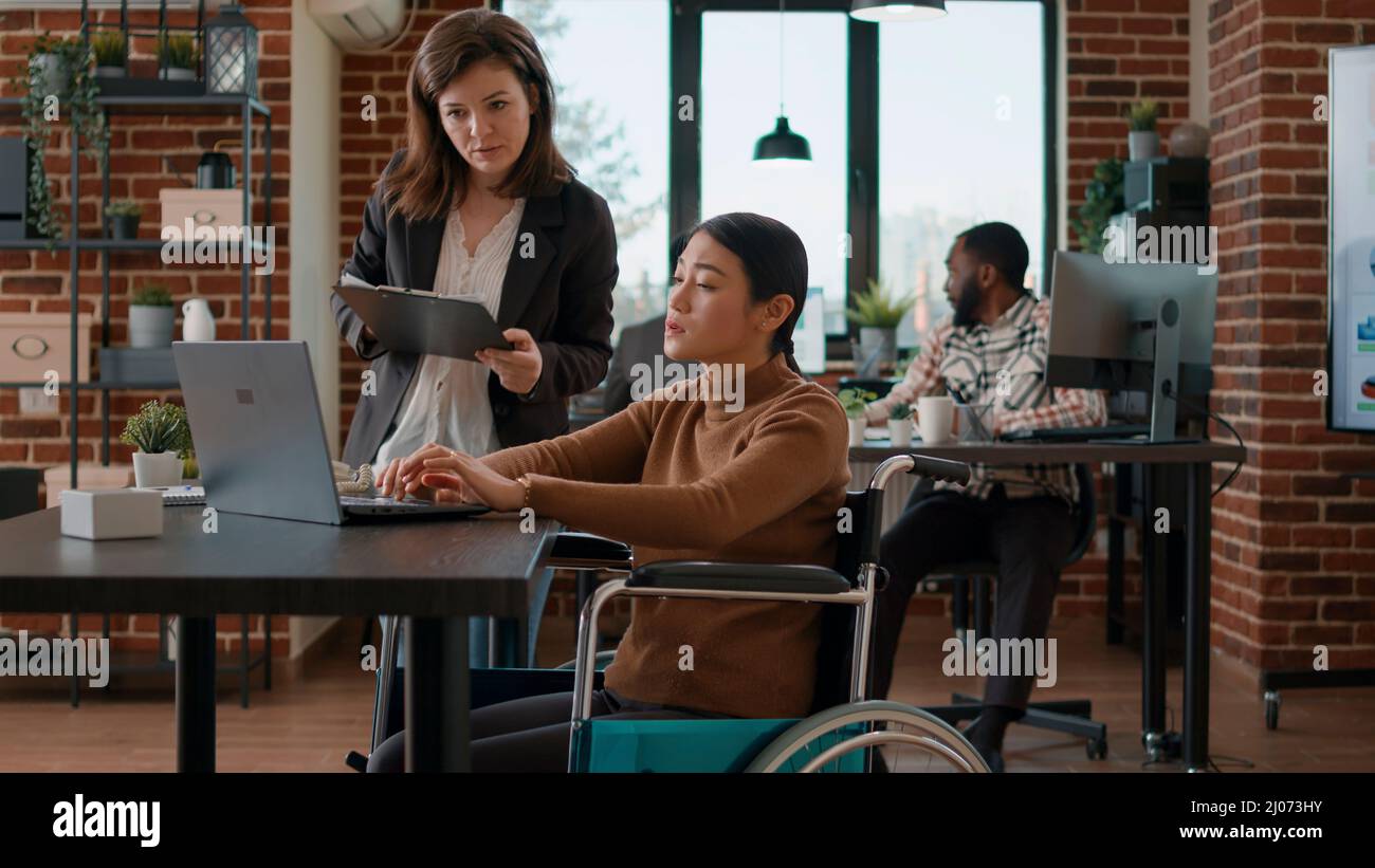 Asian woman in wheelchair brainstorming ideas with colleague, doing ...