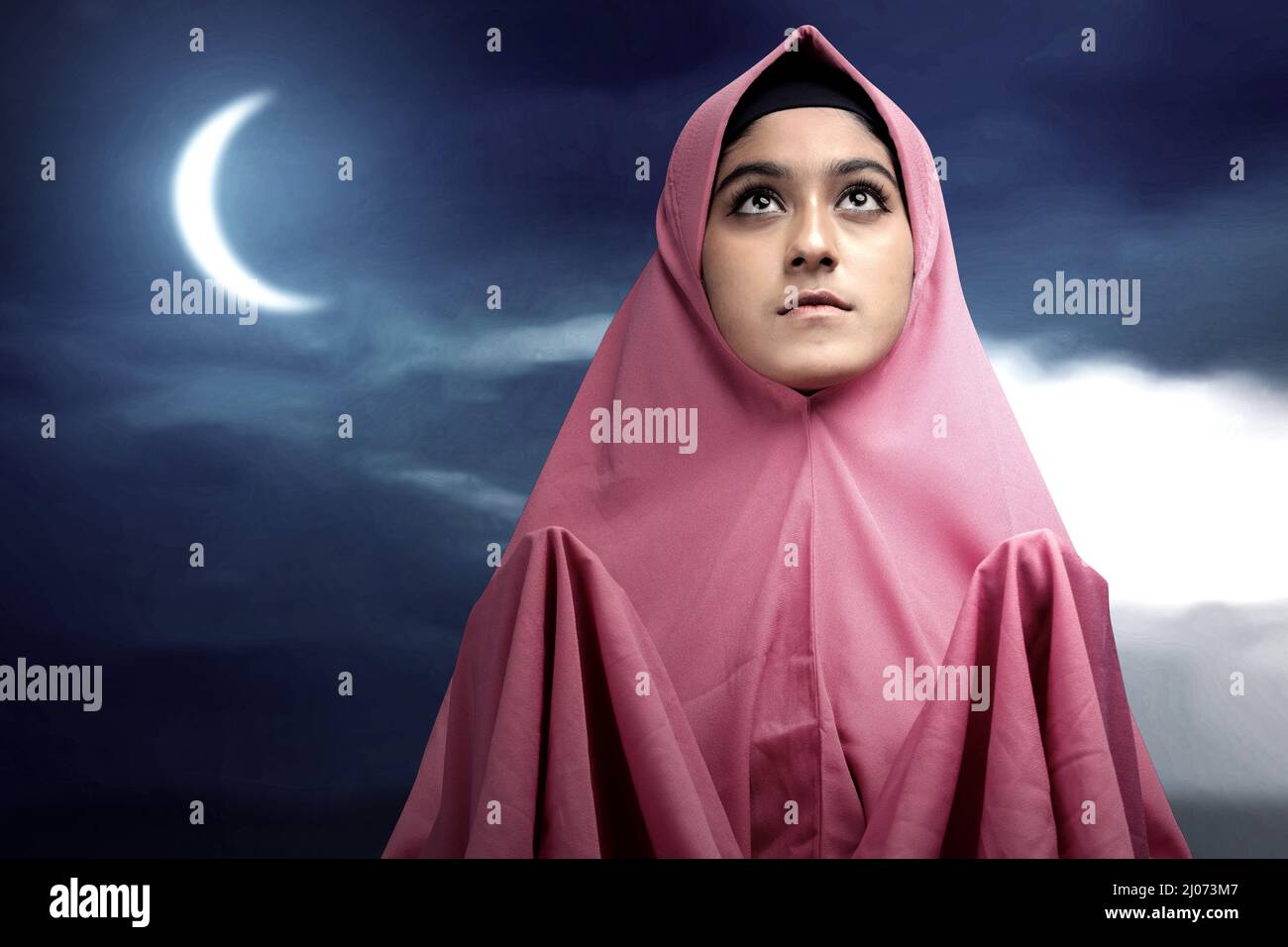Asian Muslim woman in a veil standing while raised hands and praying ...