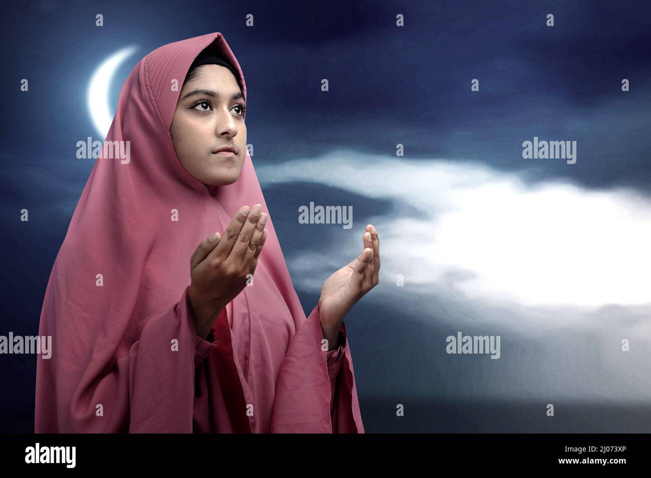 Asian Muslim woman in a veil standing while raised hands and praying ...