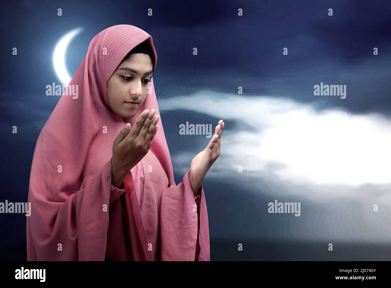 Asian Muslim woman in a veil standing while raised hands and praying ...