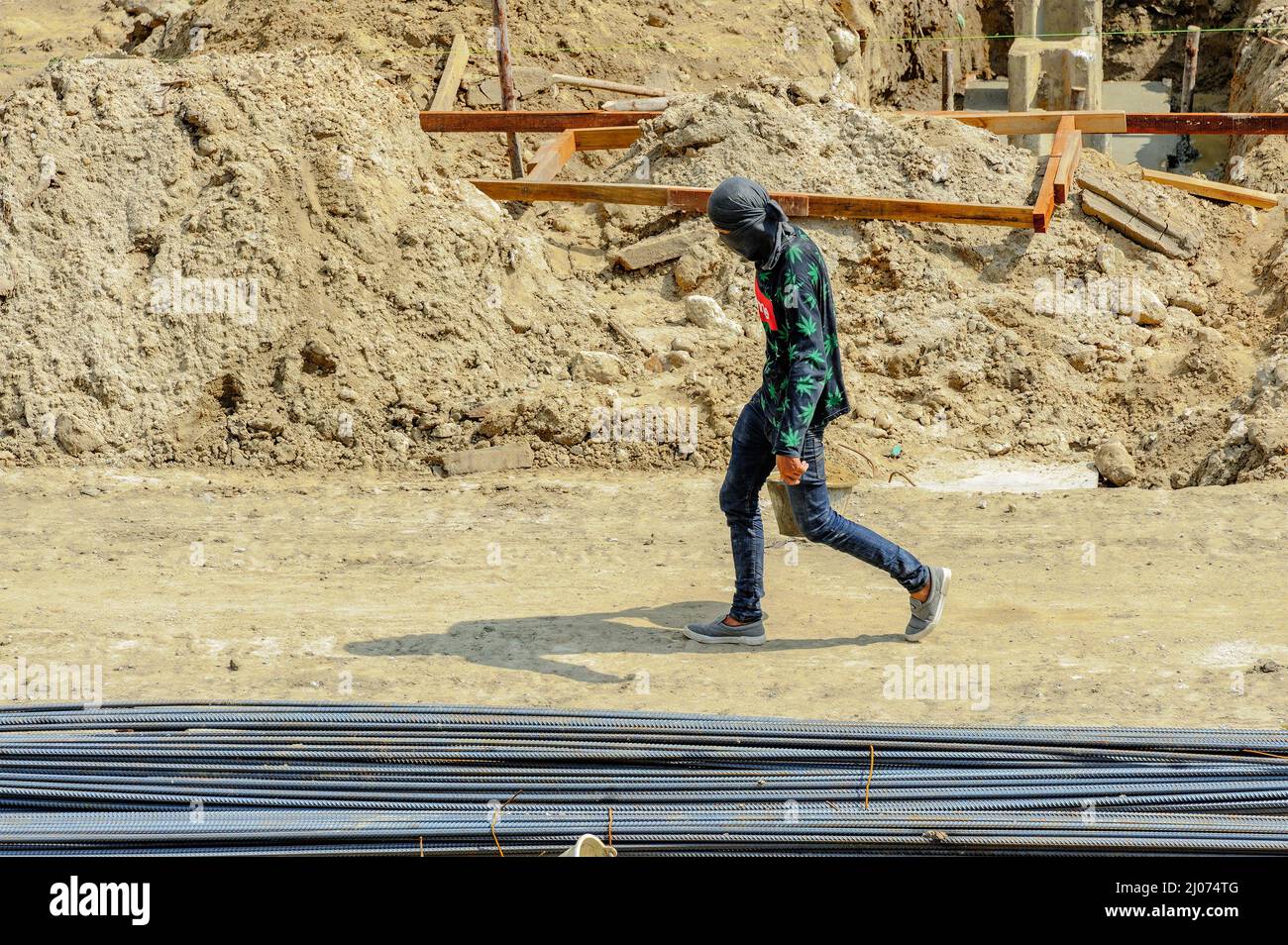 A construction worker on site carrying a bucketful of sand walks hastily in the scorching sun. Stock Photo