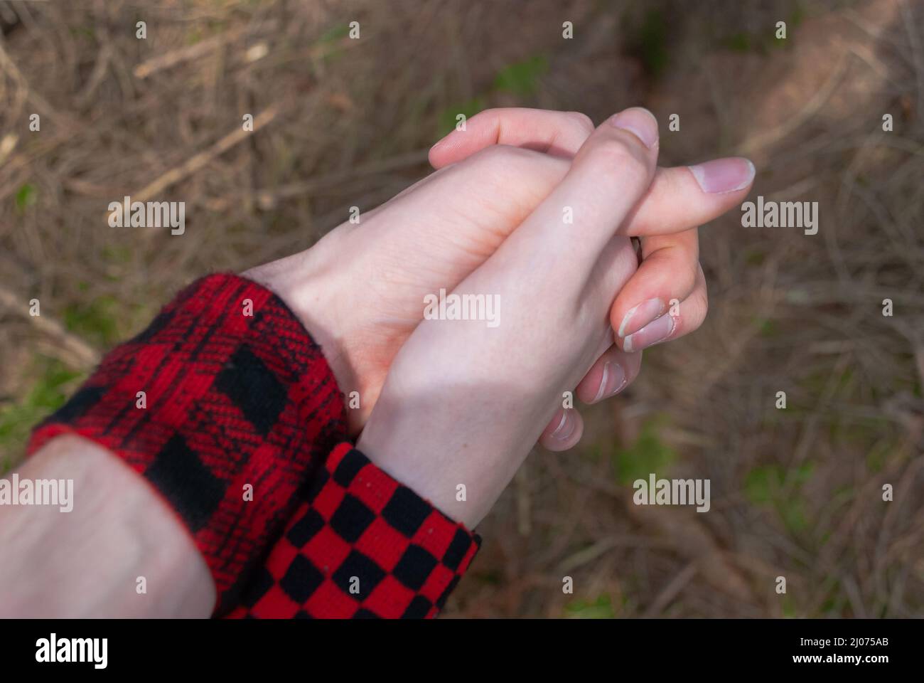 Punk emo couple holding hands, wearing red checkered armbinde while walking outdoors in the forest, close-up Stock Photo