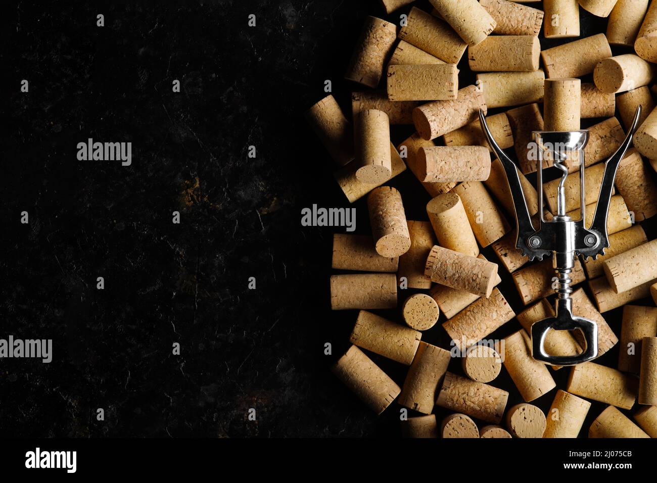 Metal corkscrew for opening wine corks against background of wine corks