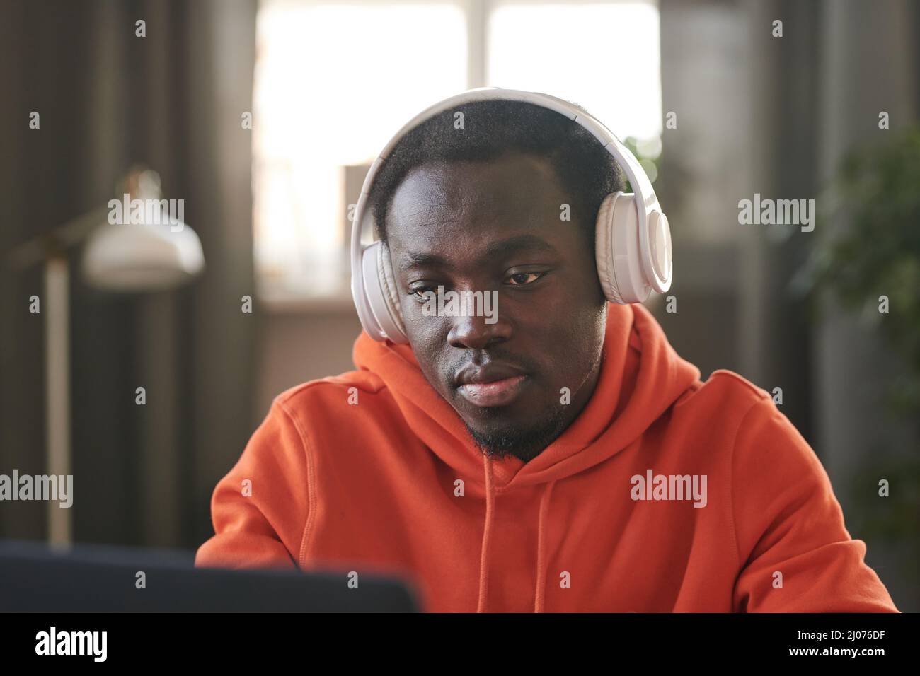 Horizontal medium close-up portrait of handsome young African American man wearing white headphones surfing internet on laptop Stock Photo