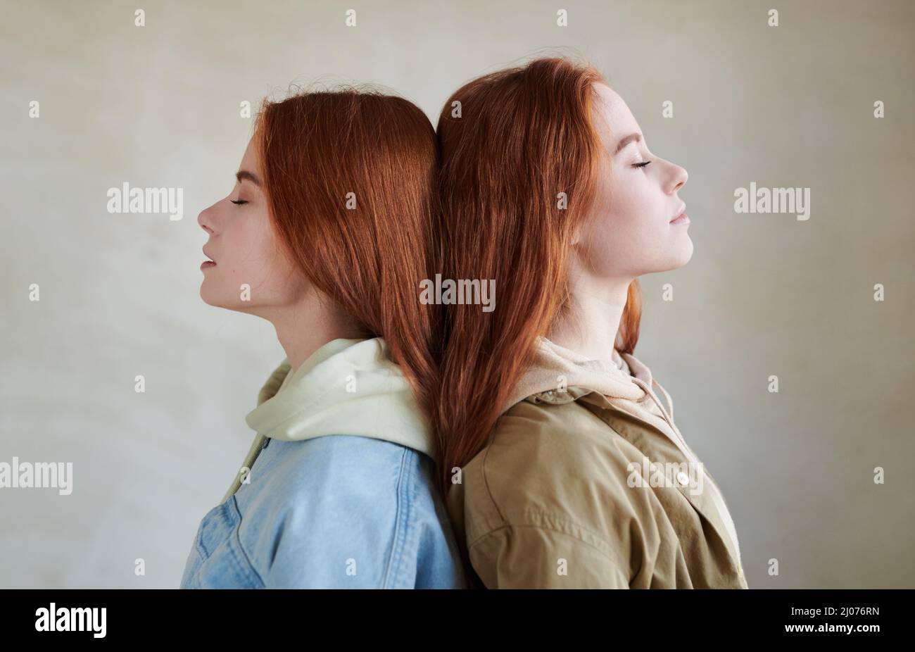 Medium close-up side view studio portrait of two beautful red-haired sisters standing with eyes closed head to head Stock Photo