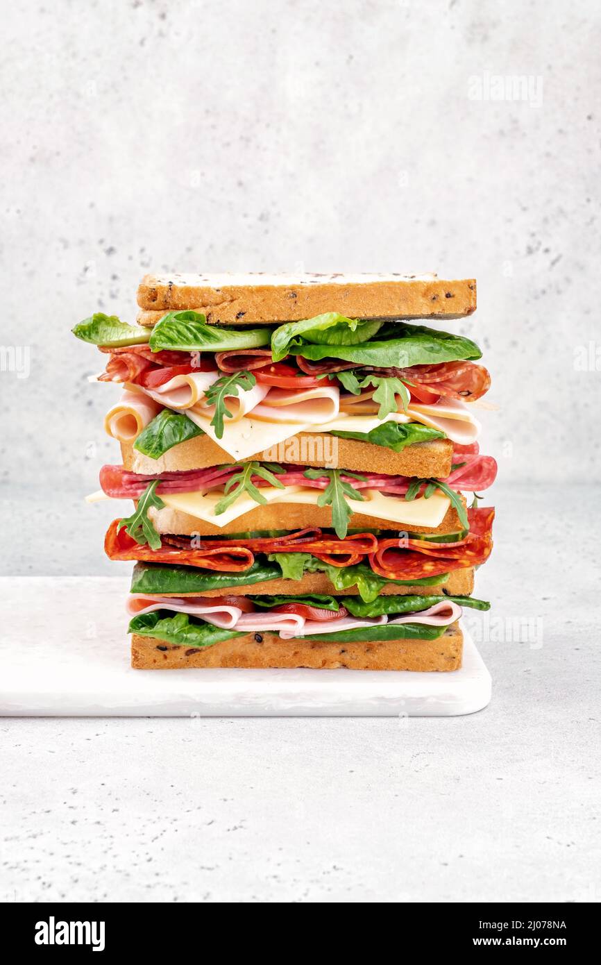 Big tasty sandwich with ham, salami, salad, cheese and tomatoes Stock Photo
