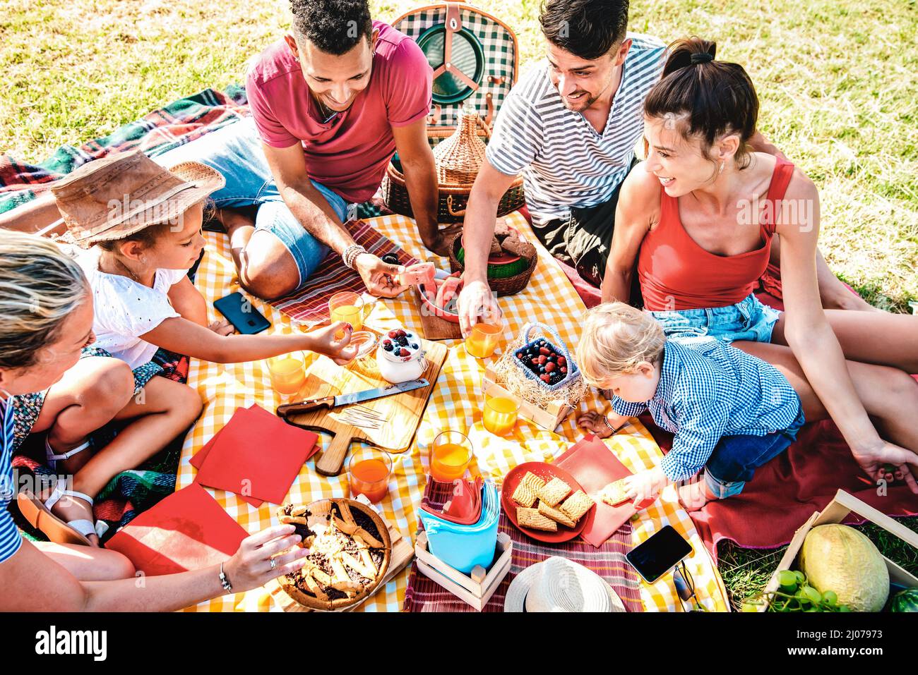 Multiracial families having fun together with kids at park on pic nic party - Genuine joy and love life style concept with mixed age people toasting j Stock Photo