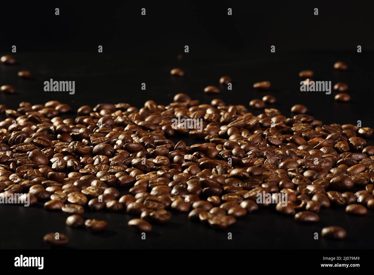 Scattered shiny roasted coffee beans on a black background with copy ...