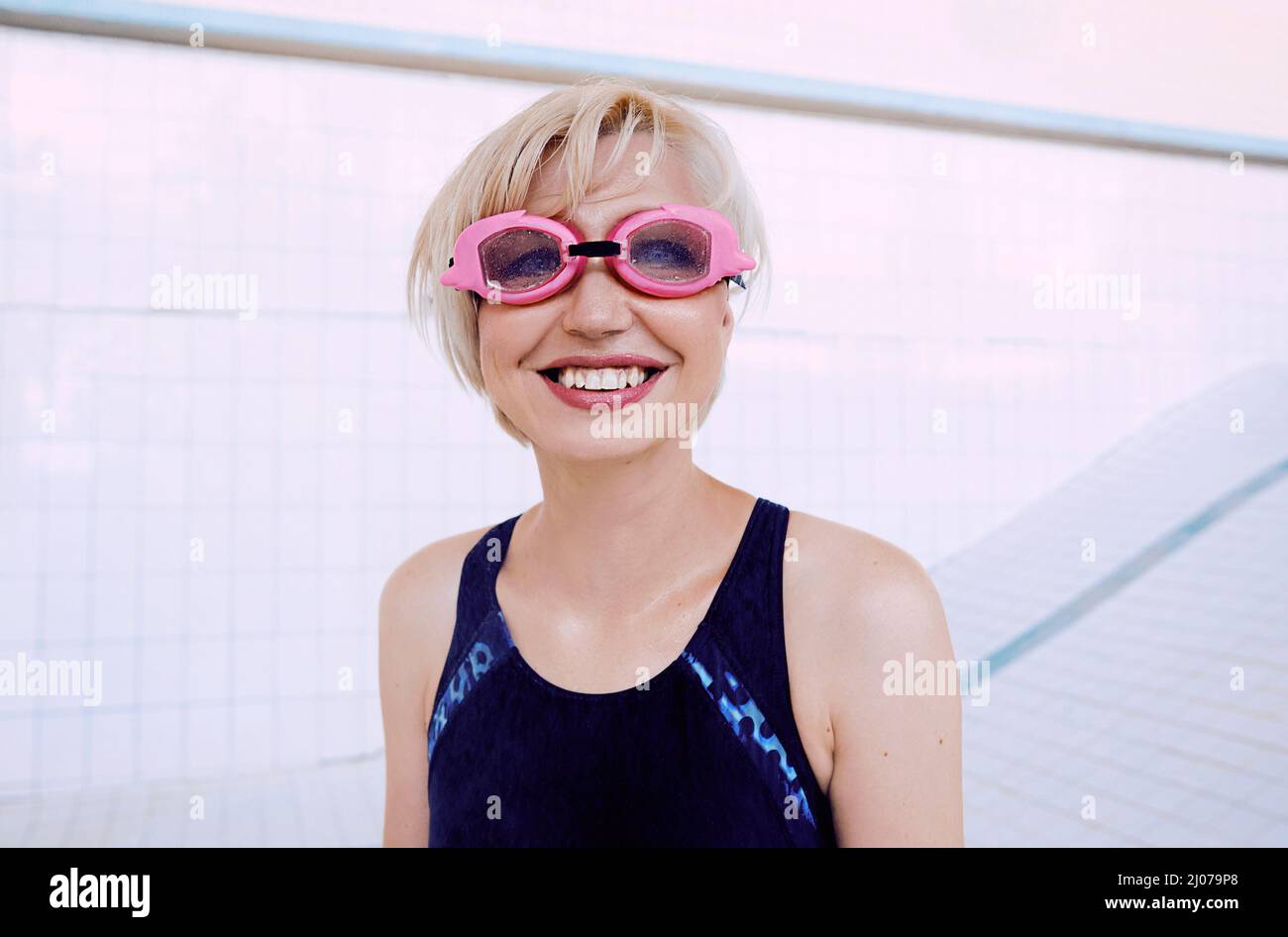 portrait of young woman in swimsuit and swimming goggles standing in the empty swimming pool and smiling Stock Photo