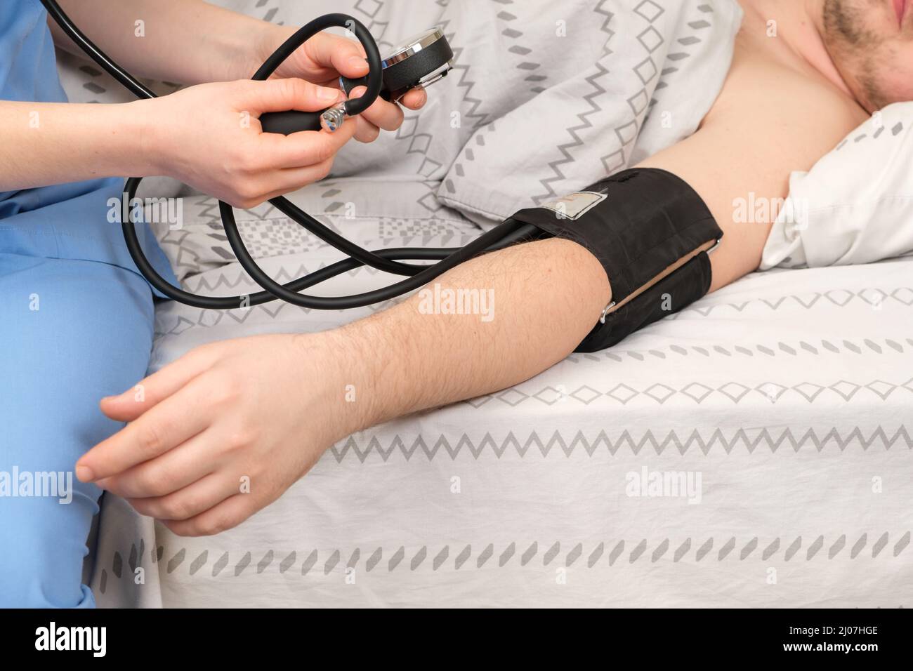 The doctor measures the blood pressure of man lying in bed. Diseases of the heart and blood vessels in humans, mechanical tonometer close up. Stock Photo