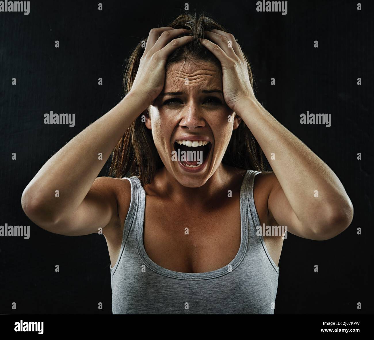 Make it go away. A young woman screaming uncontrollably while isolated on a black background. Stock Photo