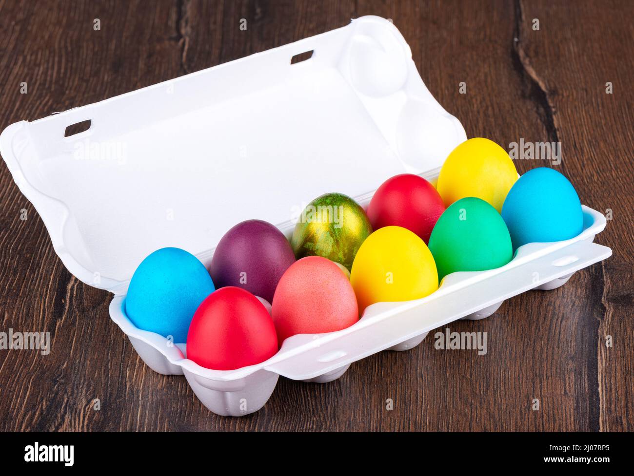 Multi-colored Easter eggs in a white plastic package on a wooden background. Close up. Stock Photo