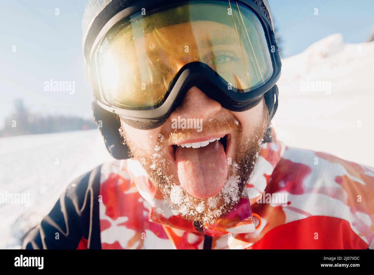 Portrait smile young bearded man with fresh snow holding snowboard background of ski resort lift, sun light. Stock Photo