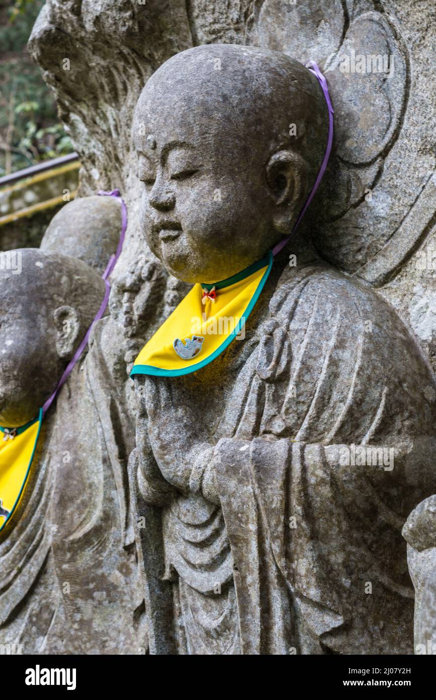 Close up detail of a Japanese gray stone buddha statue with a yellow bib at Kurama-dera temple in Kyoto Japan Stock Photo