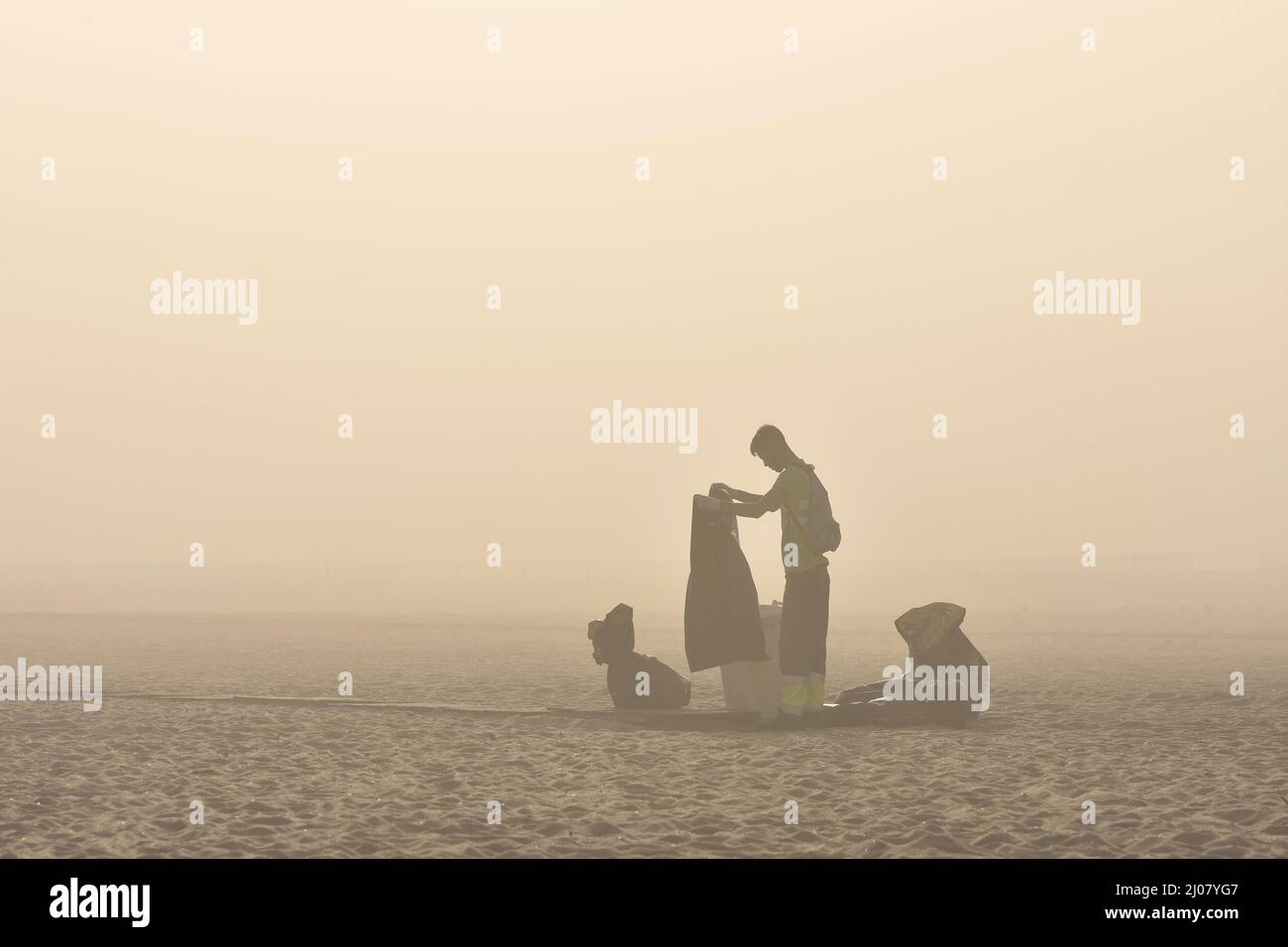 Man cleaning the beach, changing rubbish bags in morning fog, Figueira da Foz Portugal. Stock Photo