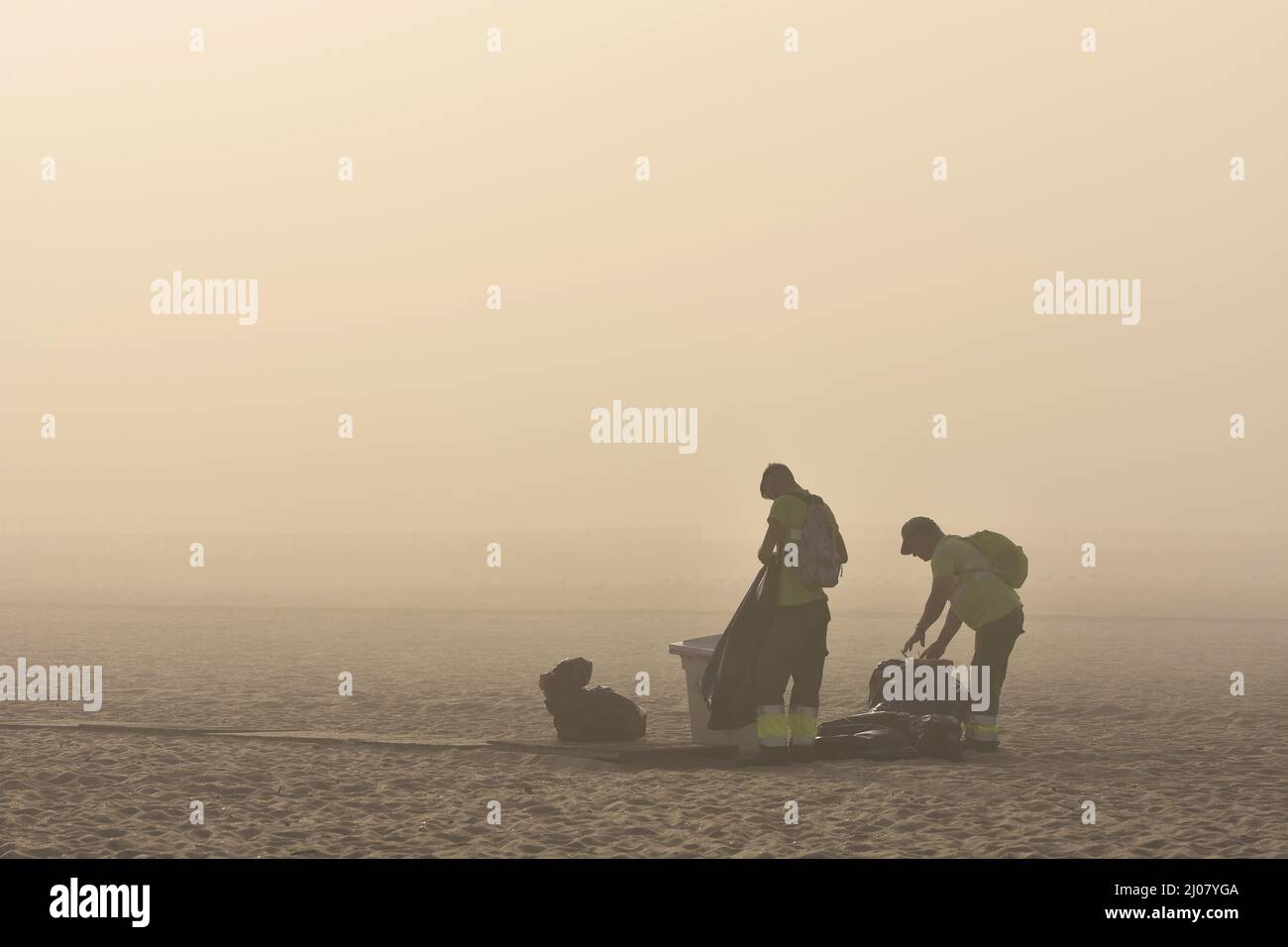 Men cleaning the beach, changing rubbish bags in morning fog, Figueira da Foz Portugal. Stock Photo