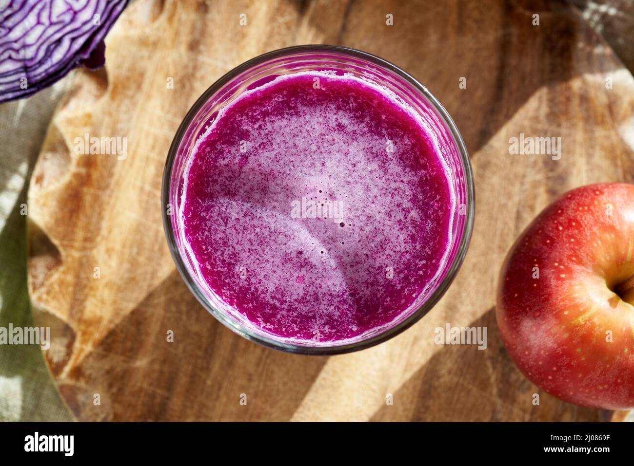 Homemade purple cabbage juice in a glass, with fresh apples, top view