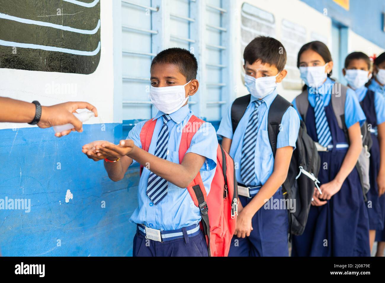 School kids with medical face mask being test with temperature and applying sanitizer before entering to class - concept of coronavirus covid-19 Stock Photo