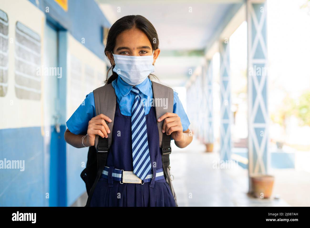 Girl kid in uniform with medical face mask standing at school corridor - concept of back to school, covid coronavirus protuction and healthcare safty Stock Photo