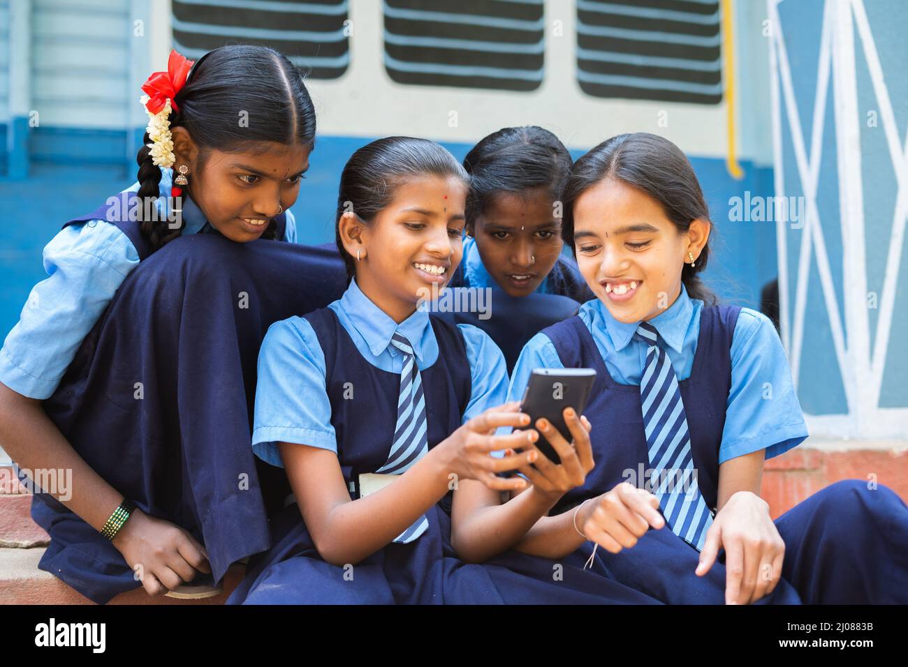 group of smiling girl kids busy using mobile phone at school corridor during break - concpet of smartphone addiction, using social media and Stock Photo