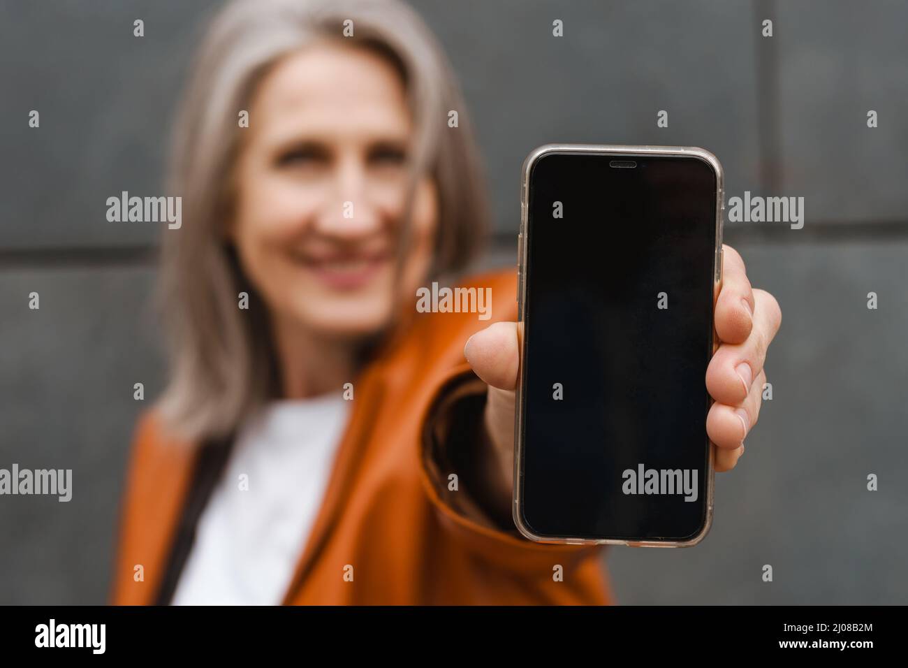 Grey senior woman smiling while showing her mobile phone outdoors Stock Photo