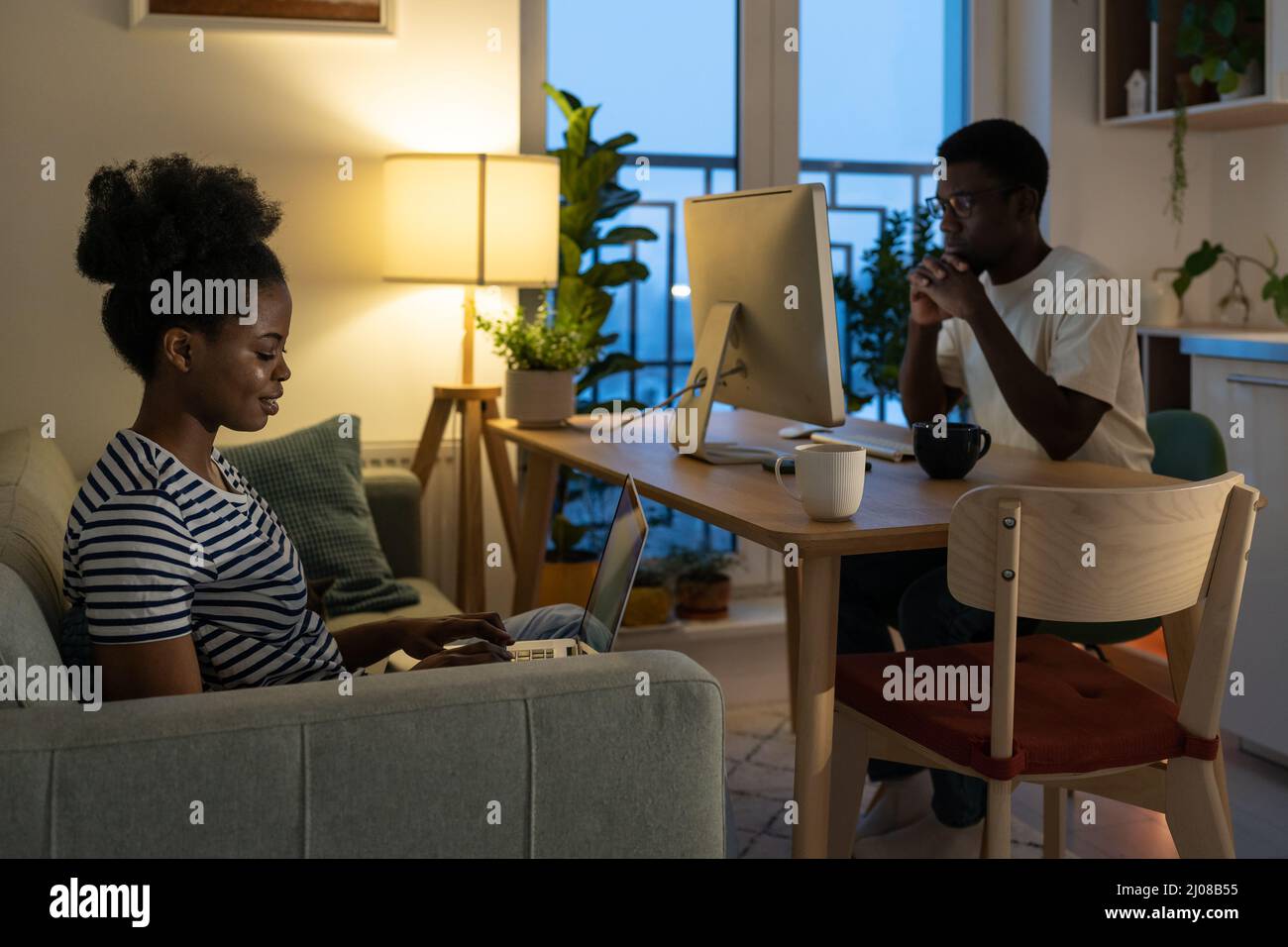 Young afro couple of freelancers work from home together busy with projects use computer and laptop Stock Photo