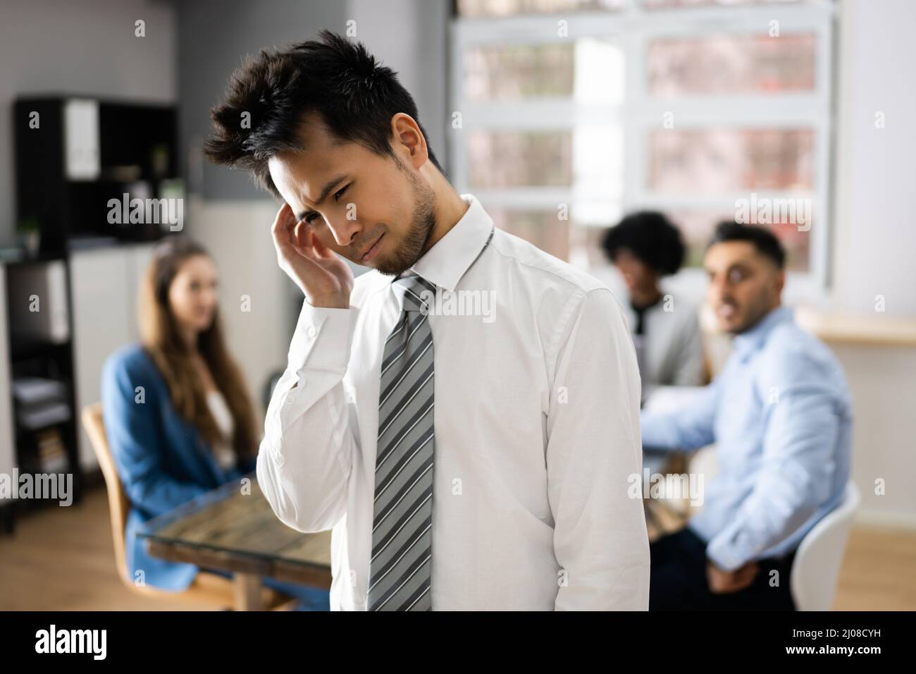 Stressed Asian Colleague And Other Workers Bullying In Office Stock Photo
