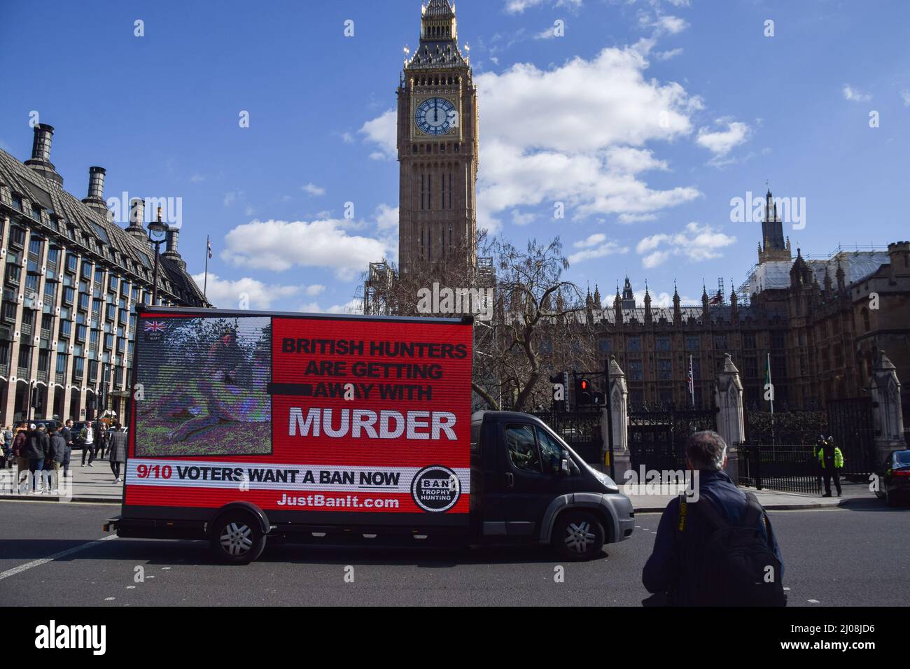London, UK. 17th Mar, 2022. An advertising van passes by Houses of Parliament with a digital screen showing an image of a hunter with a dead lion and the words 'British hunters are getting away with murder'. The organisation Campaign to Ban Trophy Hunting is currently running the campaign in response to the UK Government's potential plans to scrap a proposed ban on trophy hunting imports. Credit: ZUMA Press, Inc./Alamy Live News Stock Photo