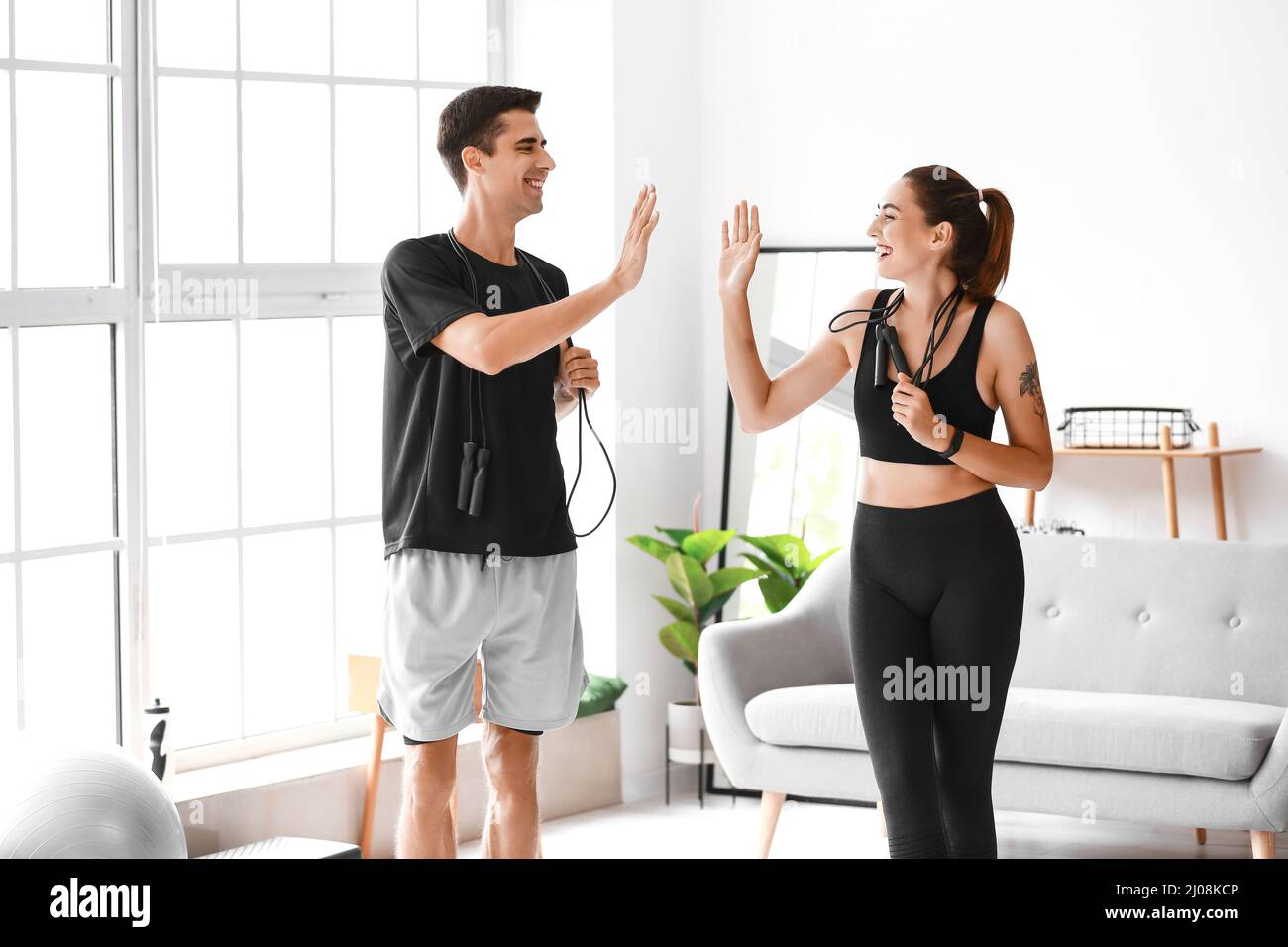 Sporty young couple with skipping ropes giving each other high-five at home Stock Photo