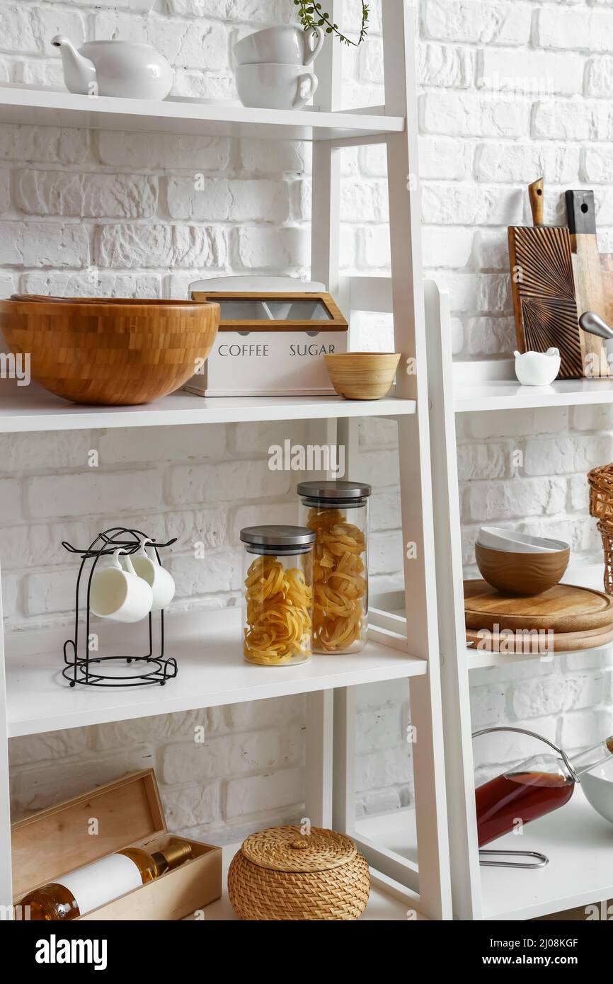 Modern shelf units with kitchenware near white brick wall Stock Photo