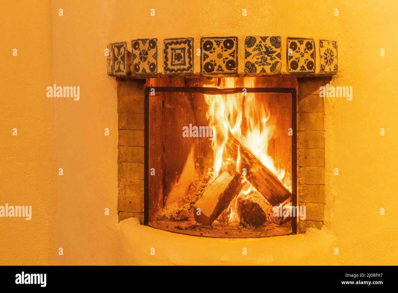 kiva style fireplace burning logs common in homes in the southwestern United States with the adobe walls radiating heat and provide cozy warmth Stock Photo