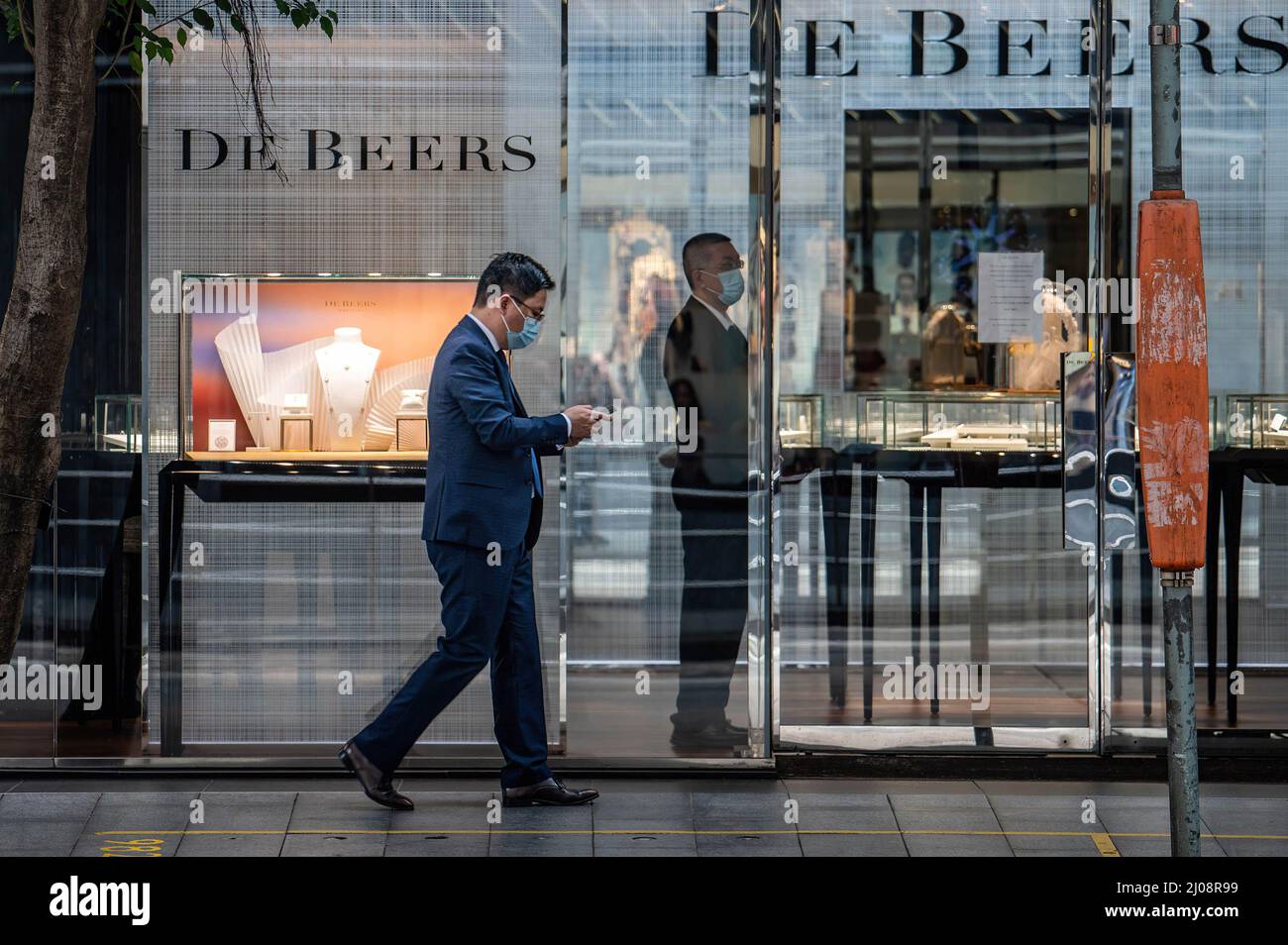 A man in a surgical mask walks by a DeBeers store in the Central Business District of Hong Kong. According to the Hong Kong Government's economic analysis, the retail sector is facing immense pressure in the near-term, with the pandemic and associated social distancing measures creating challenges for a revival. Stock Photo