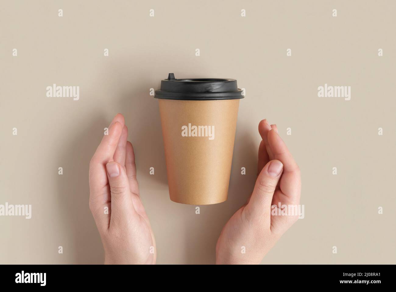 Top view of Brown coffee paper cup. Mockup with lid. Human Hands with cup for coffee or tea on beige background. Flat lay. Disposable Recycled cups Stock Photo