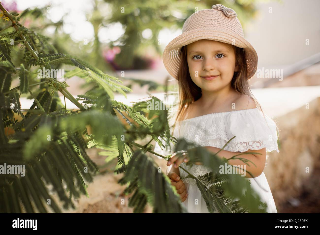 Cute little caucasian girl in a white dress and straw hat stands near a