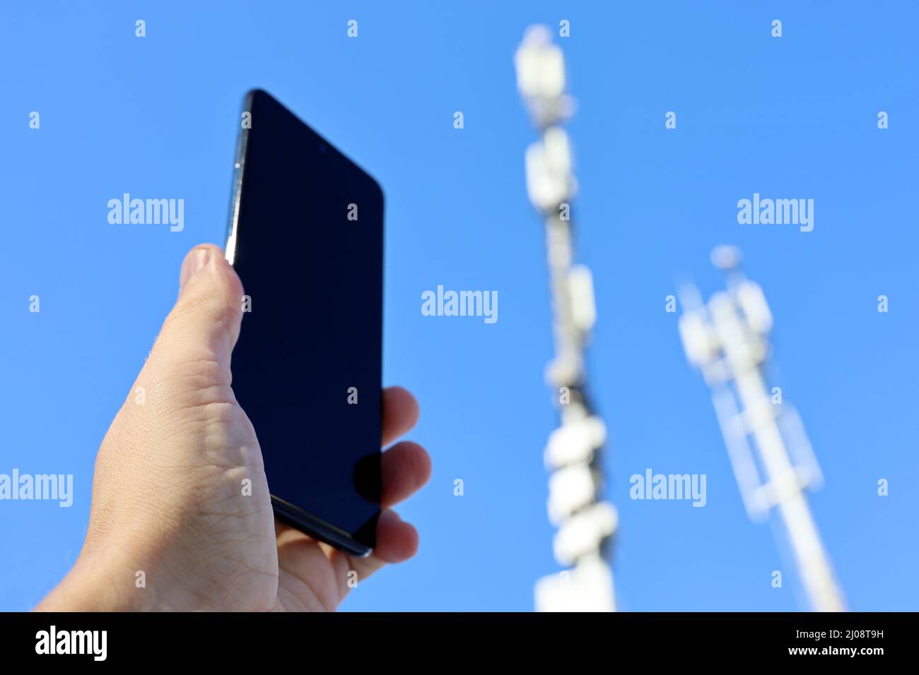 Smartphone in male hand on background of cell towers. Mobile telecommunication equipment, phone signal strength Stock Photo