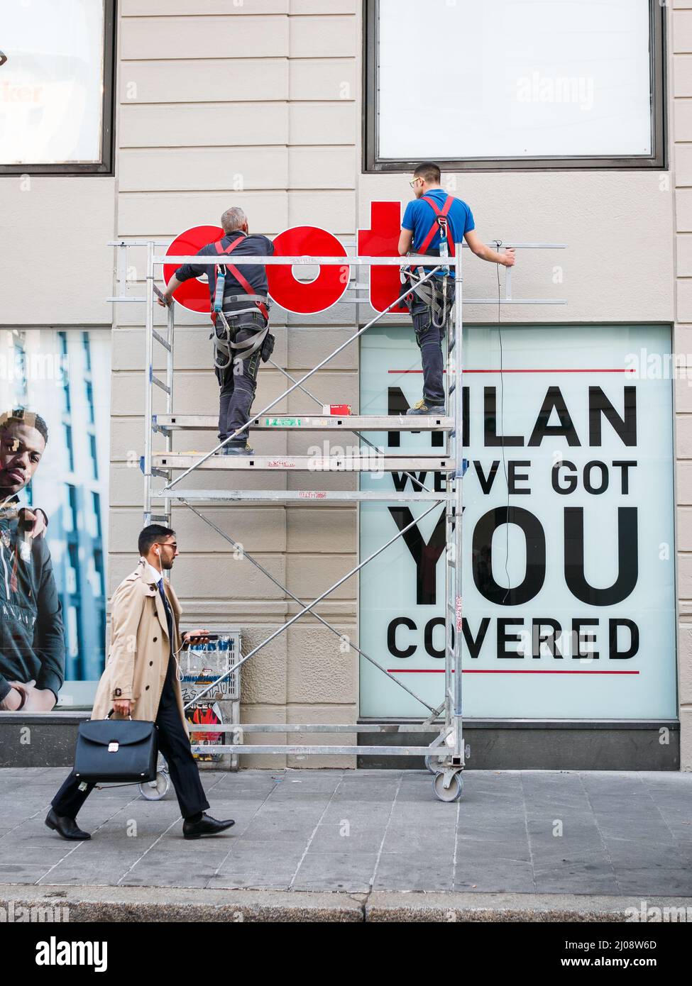 Milan, Italy. 03rd Oct, 2019. A business man walks past two men working on a business sign in Milan on March 31, 2019. Corso Buenos Aires is one of the longest shopping street in Europe and features the highest concentration of stores. (Photo by Alexander Pohl/Sipa USA) Credit: Sipa USA/Alamy Live News Stock Photo