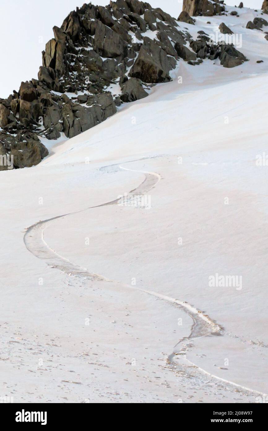 Single offpiste ski track on untouched slope covered in red sand dust cloud blown from Sahara desert by Foehn wind in early spring in Grands Montets A Stock Photo