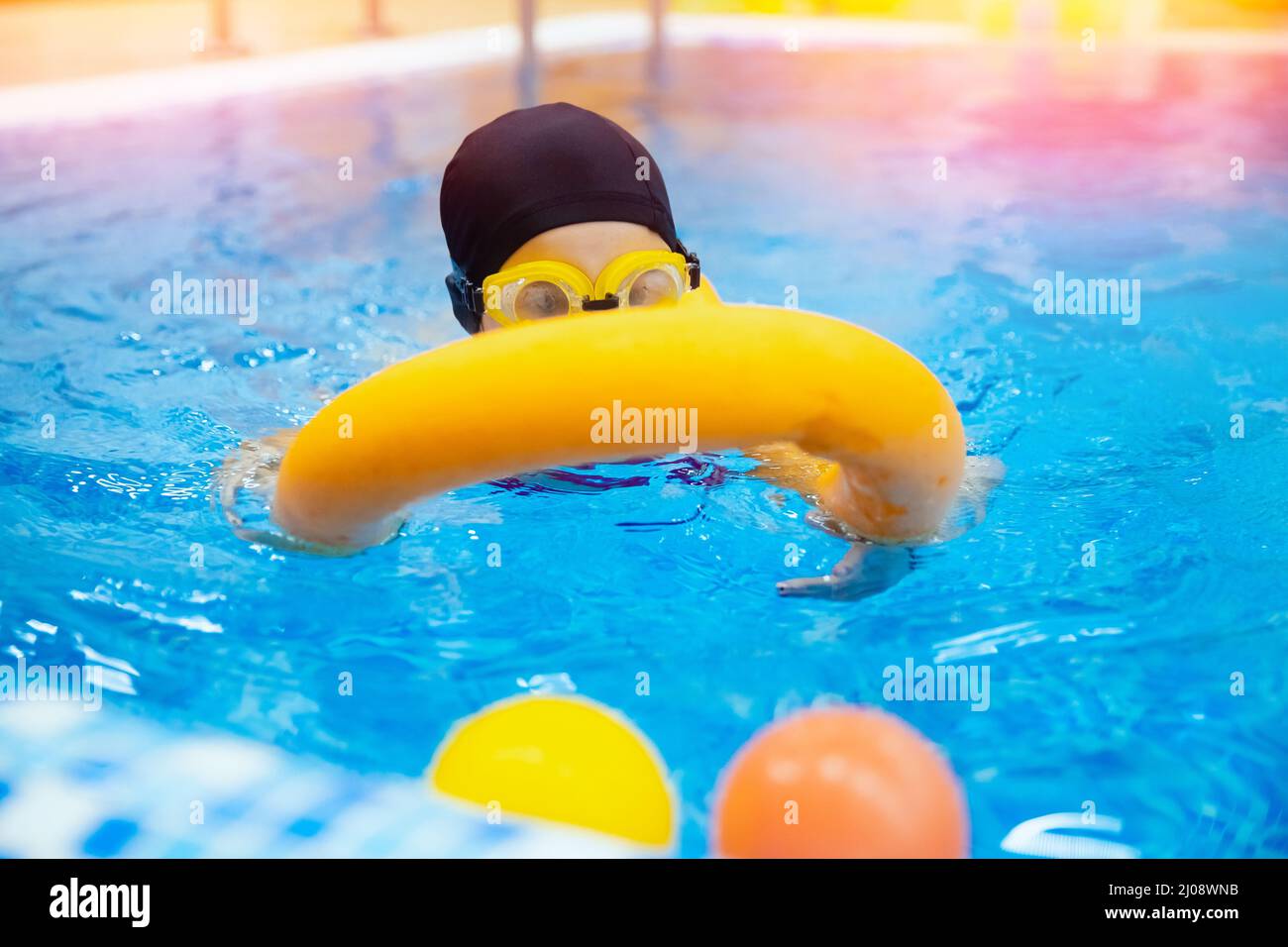 Little kid girl with glasses learning to swim with pool yellow noodle