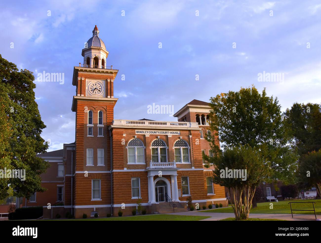 Morning sunlight illuminates the clock tower of Arkansas' Bradley County Courthouse.  Building is tan and orange bricked with a coppola topped dome. Stock Photo