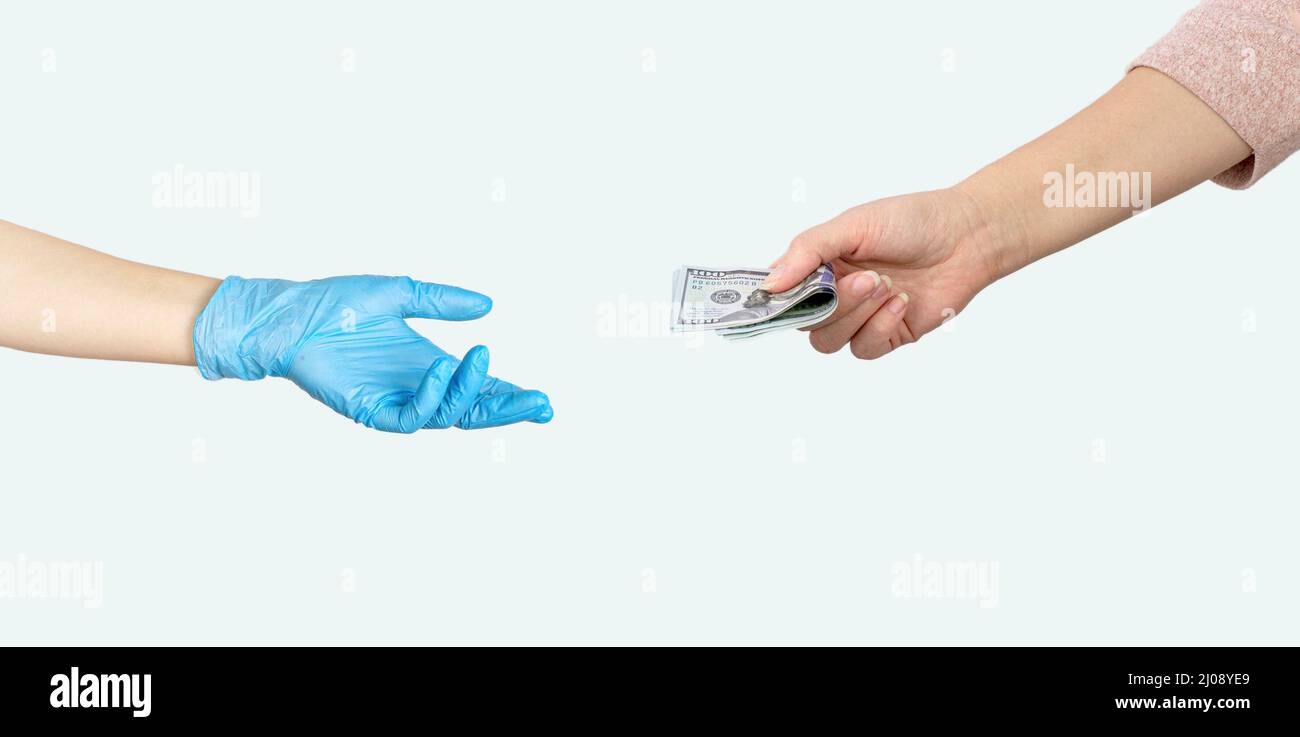 Hand giving money US dollars another hand in blue medical glove on grey background. Paid medicine. Costs for the medical insurance Stock Photo