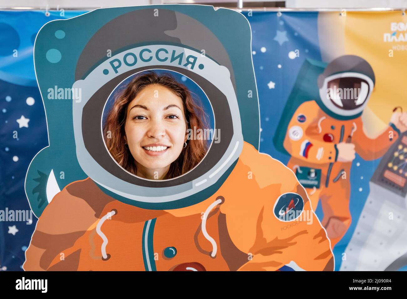 10 July 2021, Novosibirsk, Russia: Happy woman is photographed in the scenery in an astronaut's space suit with the Roscosmos label Stock Photo