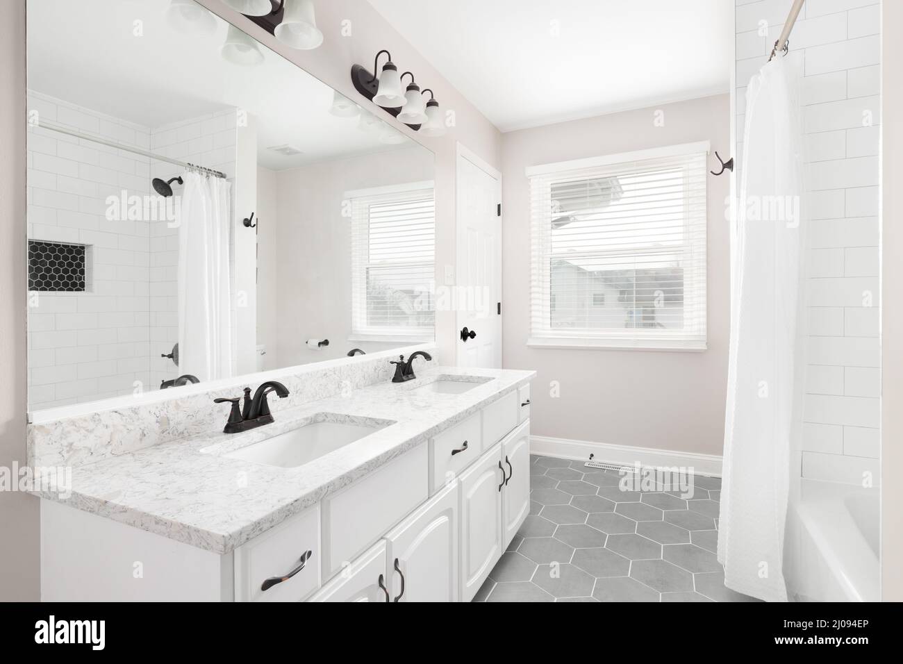 A renovated bathroom with a white vanity, grey hexagon tiled floor, marble countertop, and a