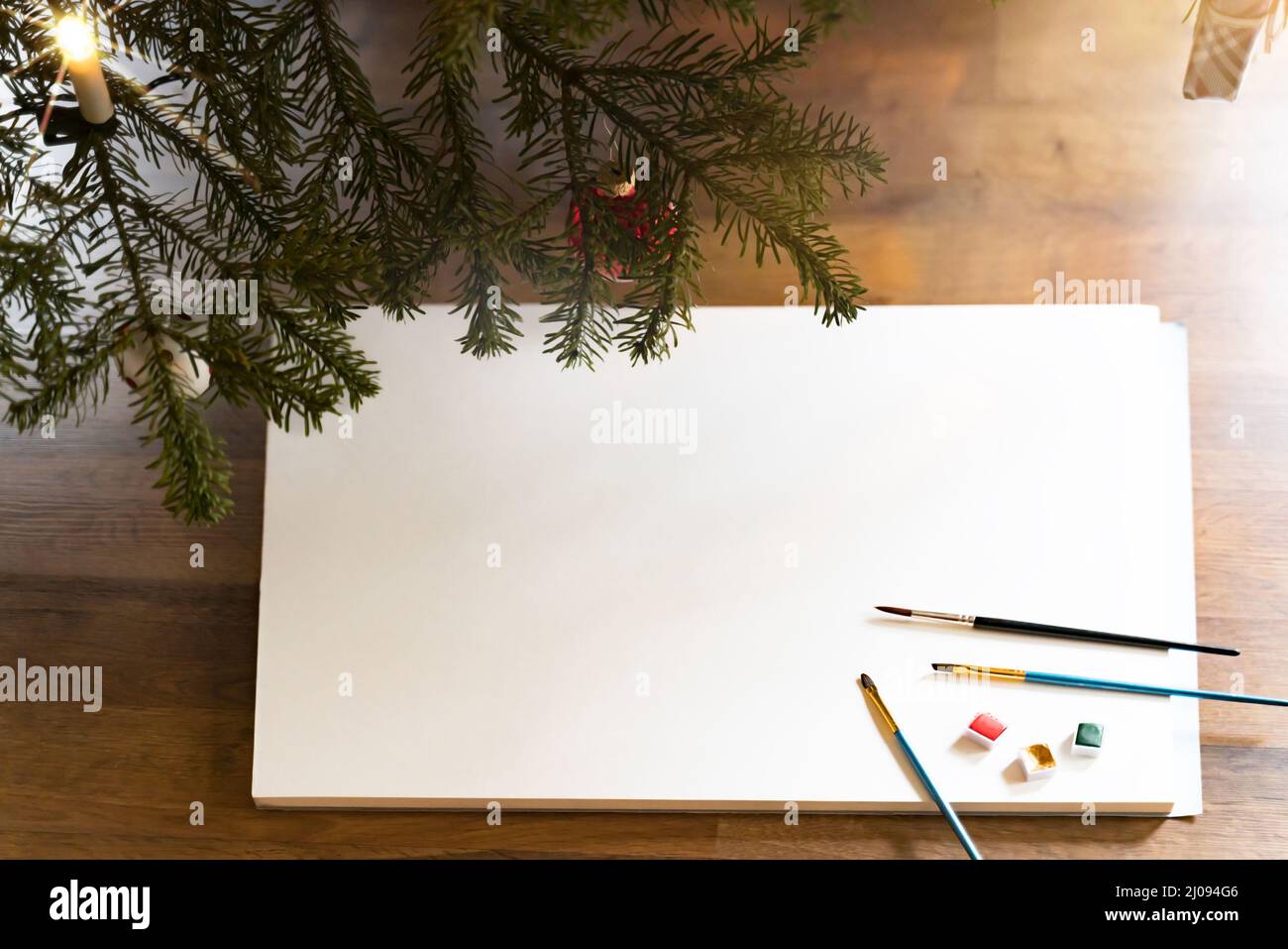 A large block of white lies under a Christmas tree. Brushes and paint pots are inviting to paint. The white area can be used for own drawings or texts Stock Photo