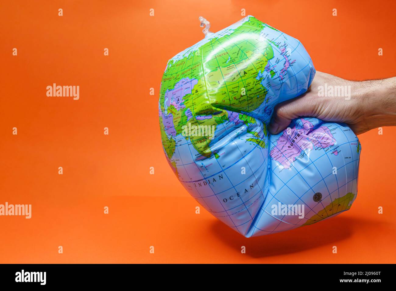 Hand tightly gripping an earth globe on orange background. Stock Photo