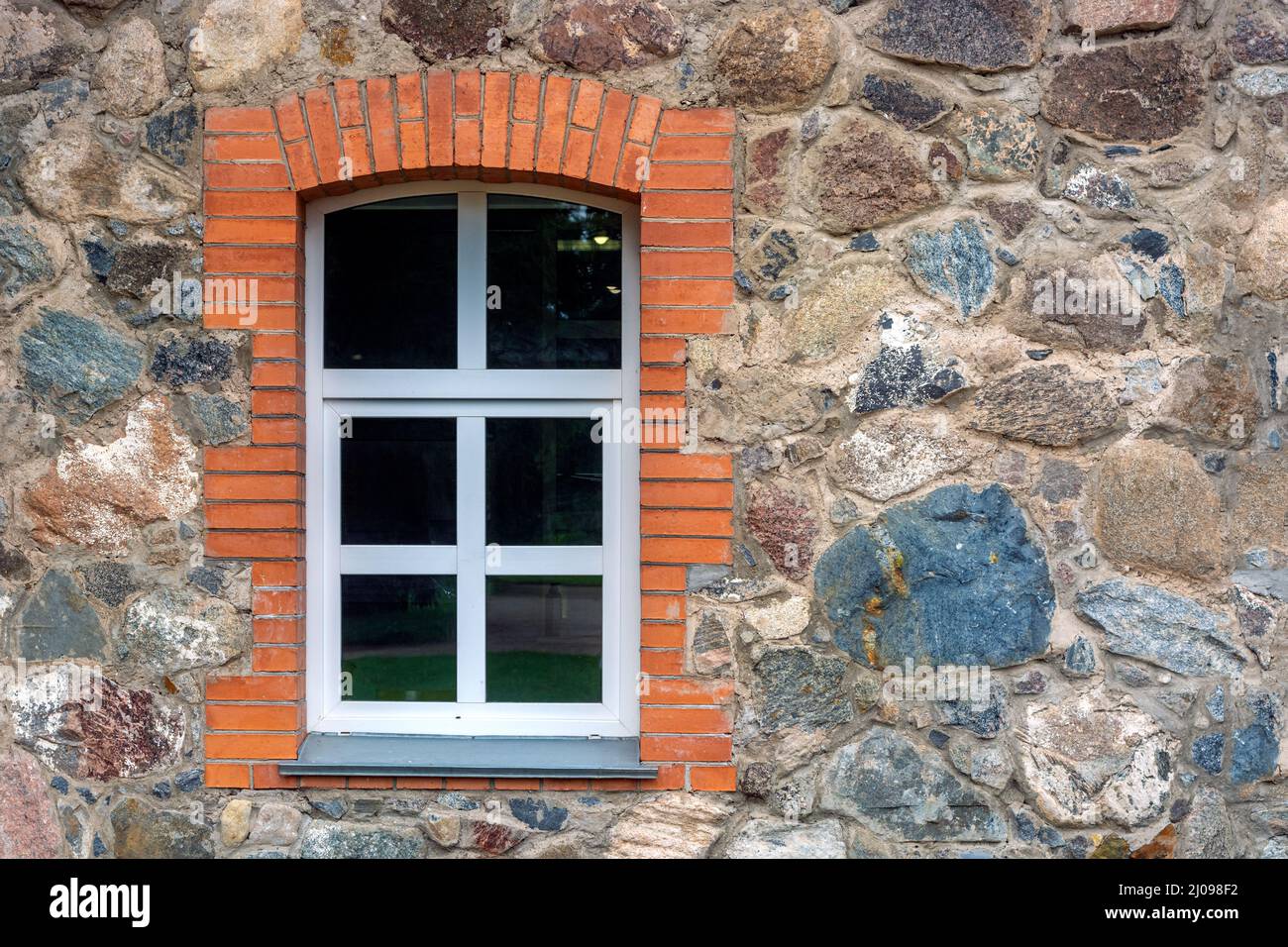 Window with a white frame framed by red brick on a stone wall. From the ...