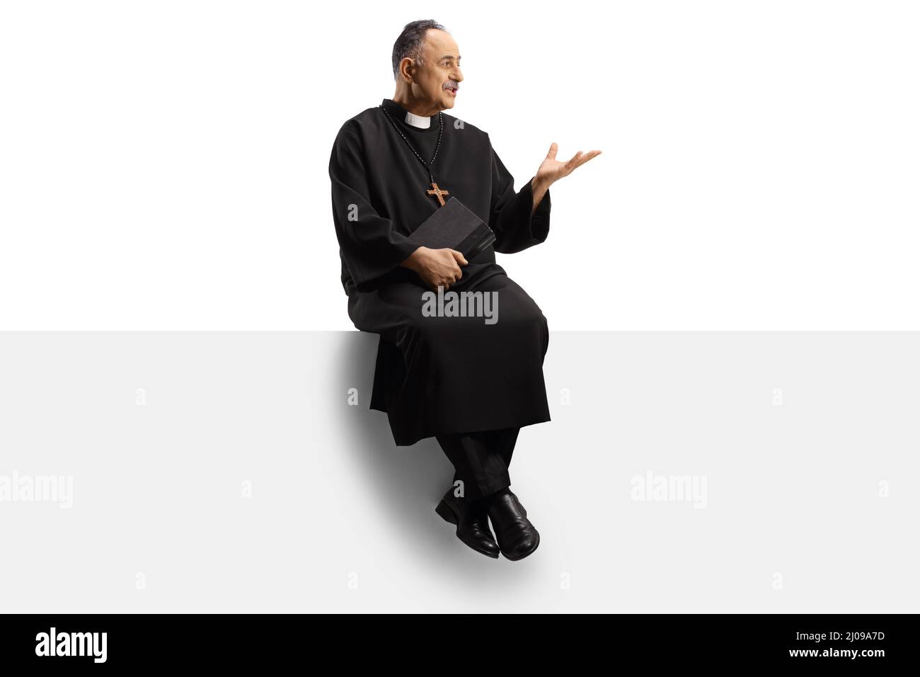 Full length shot of a mature priest sitting on a blank panel and gesturing with hand isolated on white background Stock Photo