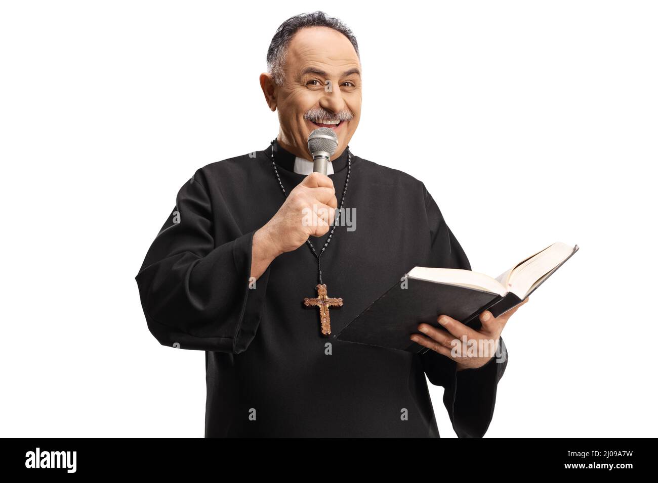 Mature priest reading a prayer from the bible and holding a microphone isolated on blue background Stock Photo