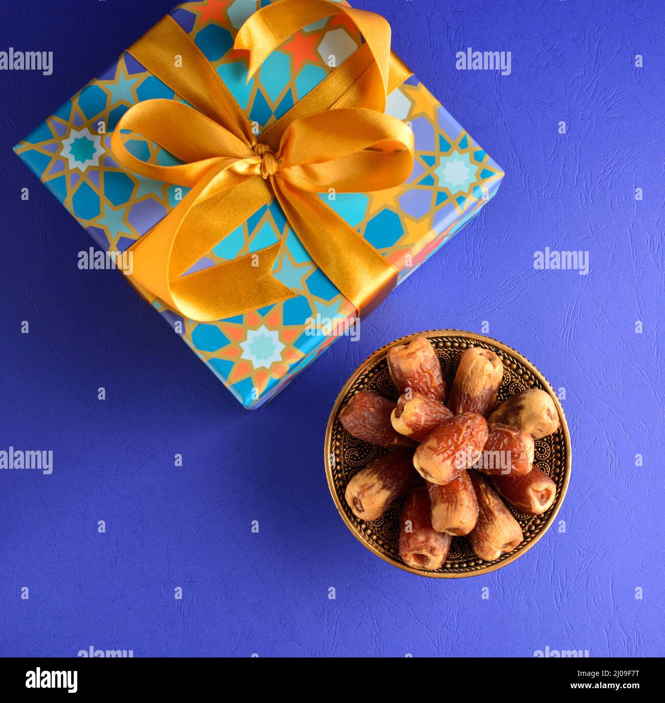 Islamic festive gift pack and date fruits. Decorative gift box for Eid occasion with golden ribbon and bowl of dates. View from top. Stock Photo